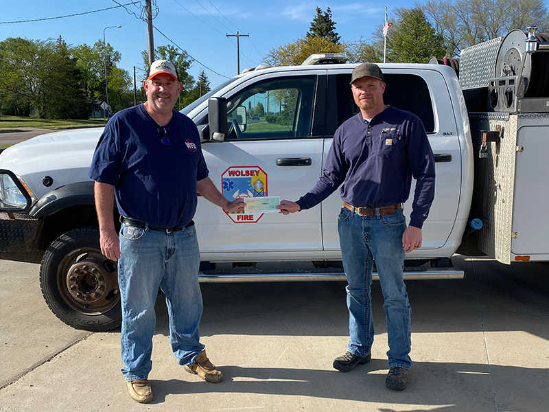 Basin Electric staff person presenting check to Wolsey Fire Department Assistant Chief in front of donated TSM truck
