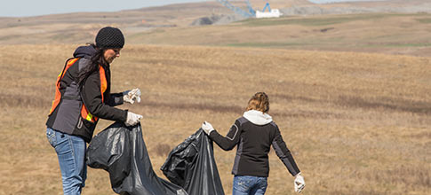 two women picking up trash in a ditch